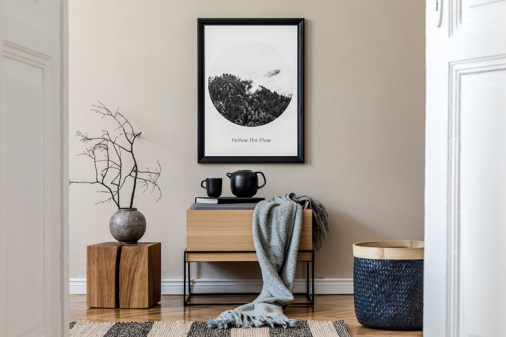 Hall inredning med sidobord, vas, tavla, svart rottingkorg, böcker och eleganta tillbehör